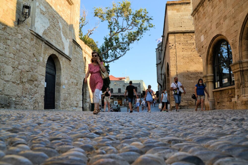 a group of people walking down a cobblestone street in the oold town of Rhodes, Greece